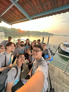 A group of people standing together with smiles at a boat jetty with the sea and a sunrise in the background.