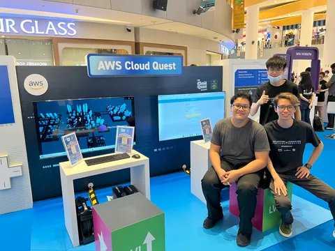 Three people sitting to the right of the screen, with the centre and left occupied by a booth titled "AWS Cloud Quest".