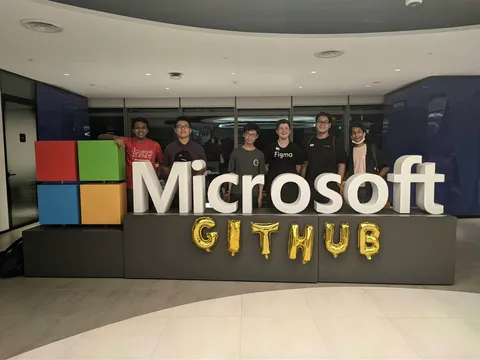 A group of six people standing in front of a logo of Microsoft with balloons spelling out GitHub below it.