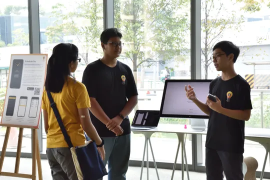 Two people standing separated by a computer presenting to another person standing across them.